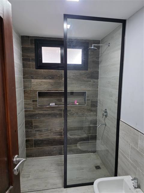 Mampara de ducha con vidrio y perfilería negra en un baño revestido símil madera